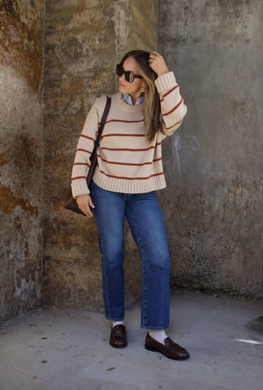 Woman wearing jeans, with a collared shirt under a sweater, and loafers