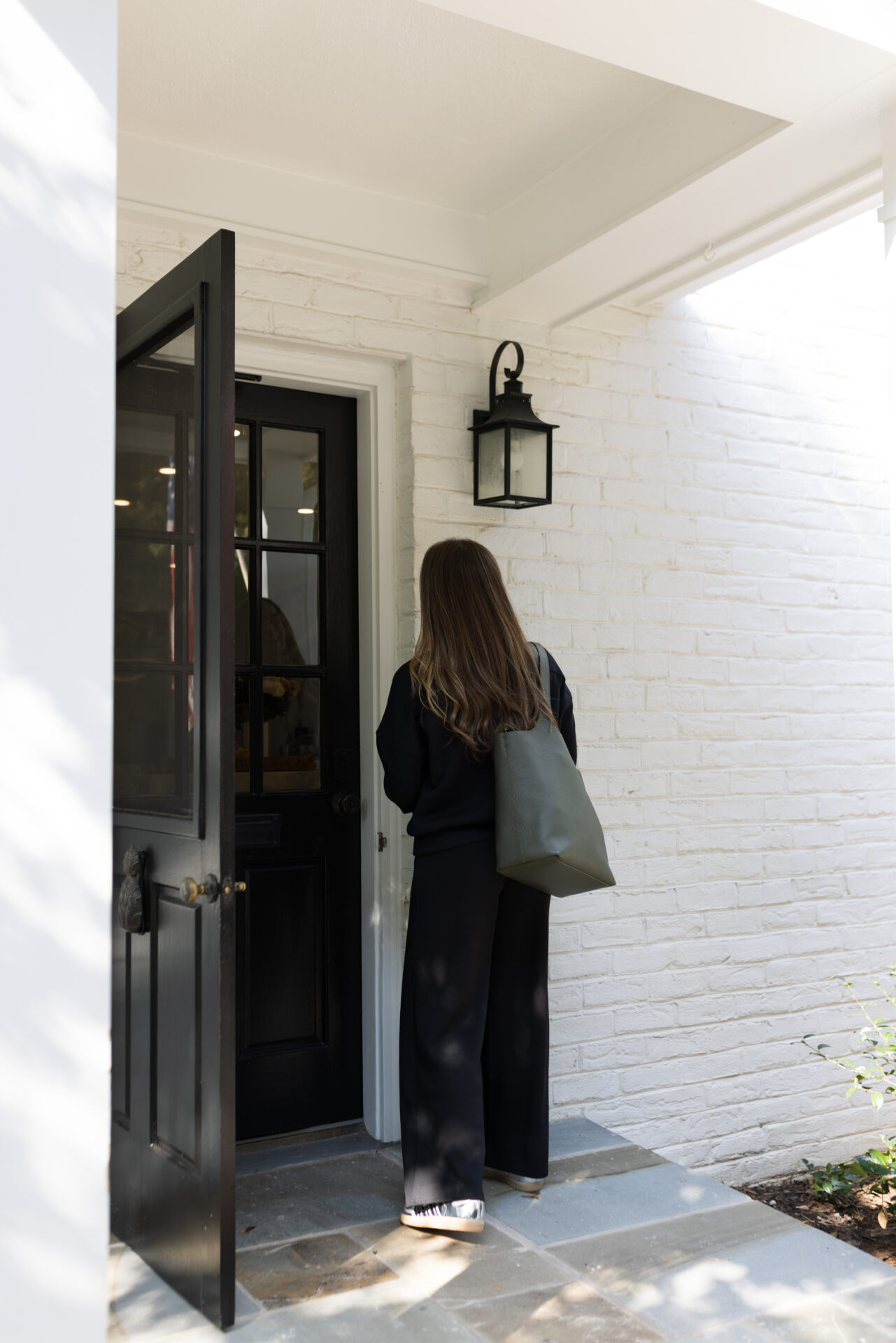 TeriLyn Adams walking into her front door in the Spanx AirEssentials set with a green tote bag