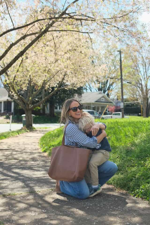 TeriLyn Adams holding son with Cuyana brown leather tote bag wearing stripe shirt and jeans