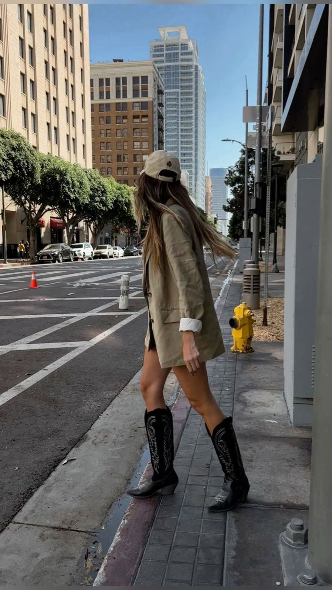 Woman wearing oversized blazer and cowboy boots walking on city street