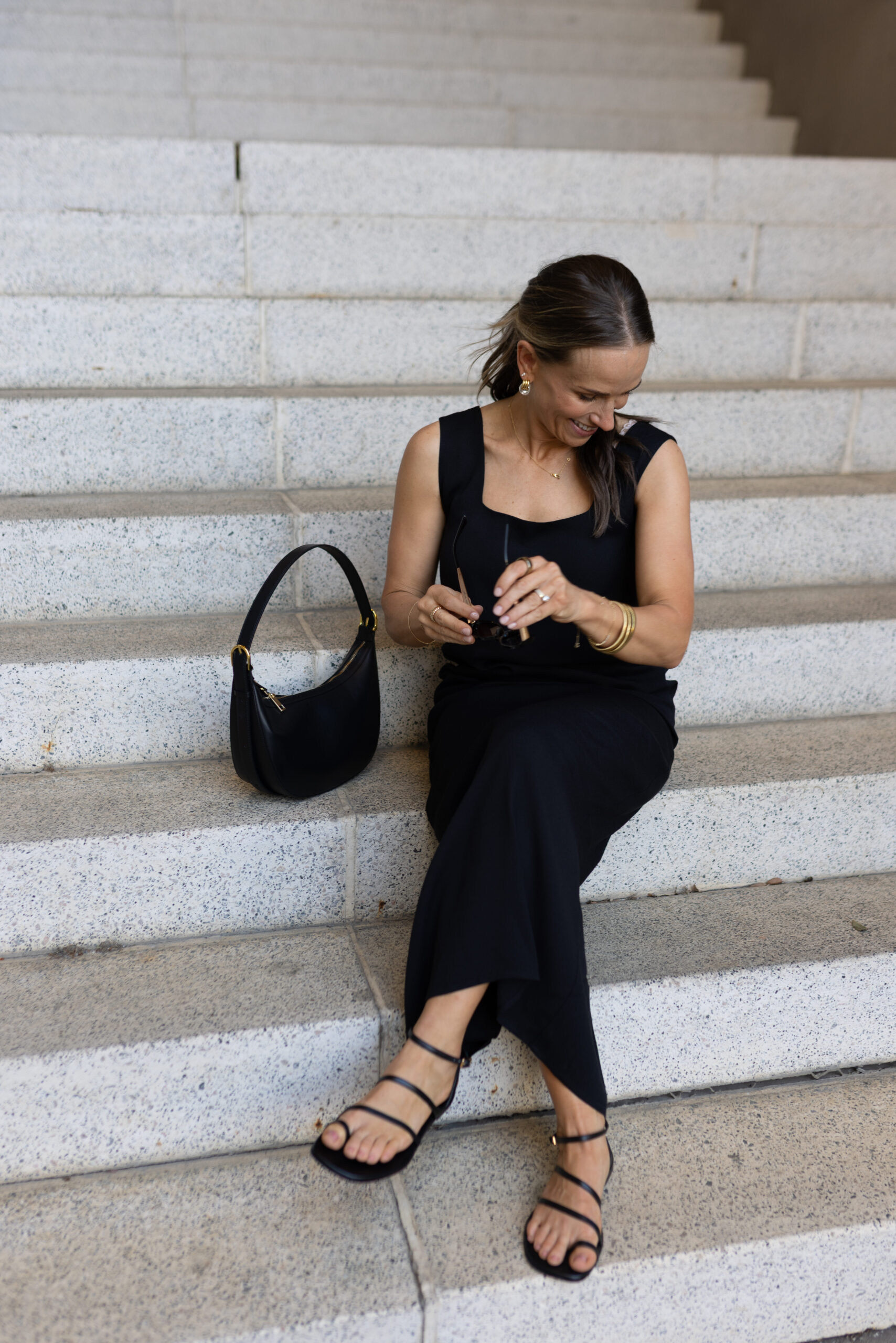 terilyn adams wearing kourt ione black maxi dress sitting on steps with black leather purse and black strappy sandals