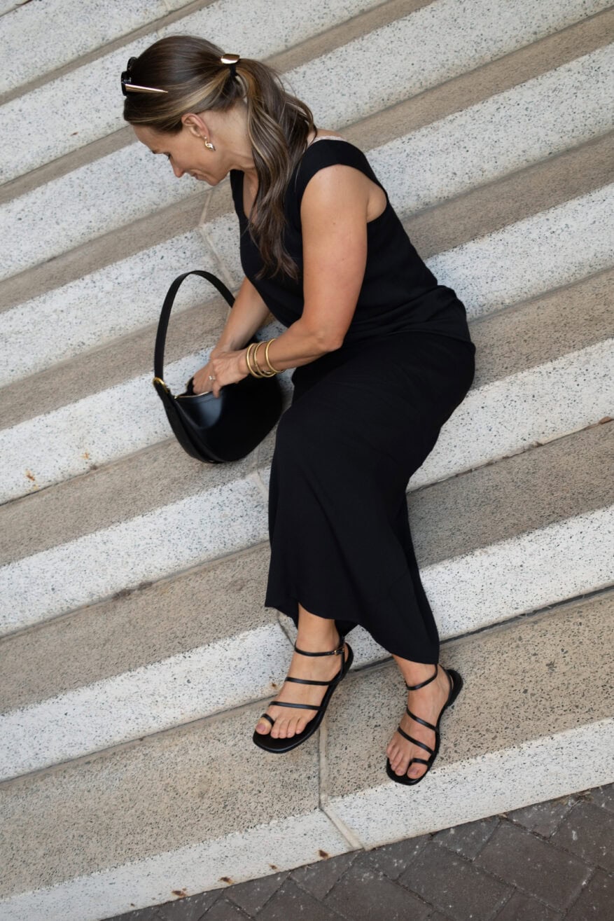 TeriLyn Adams wearing a simple black dress with gold jewelry and black strappy sandals and a black leather bag