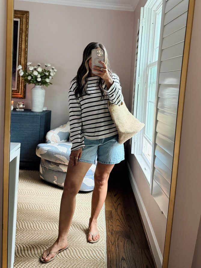 Terilyn adams taking a mirror selfie in a bright, modern room with casual outfit and handbag.
