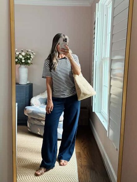 Terilyn adams taking a mirror selfie in a bright, modern room with casual outfit and handbag.