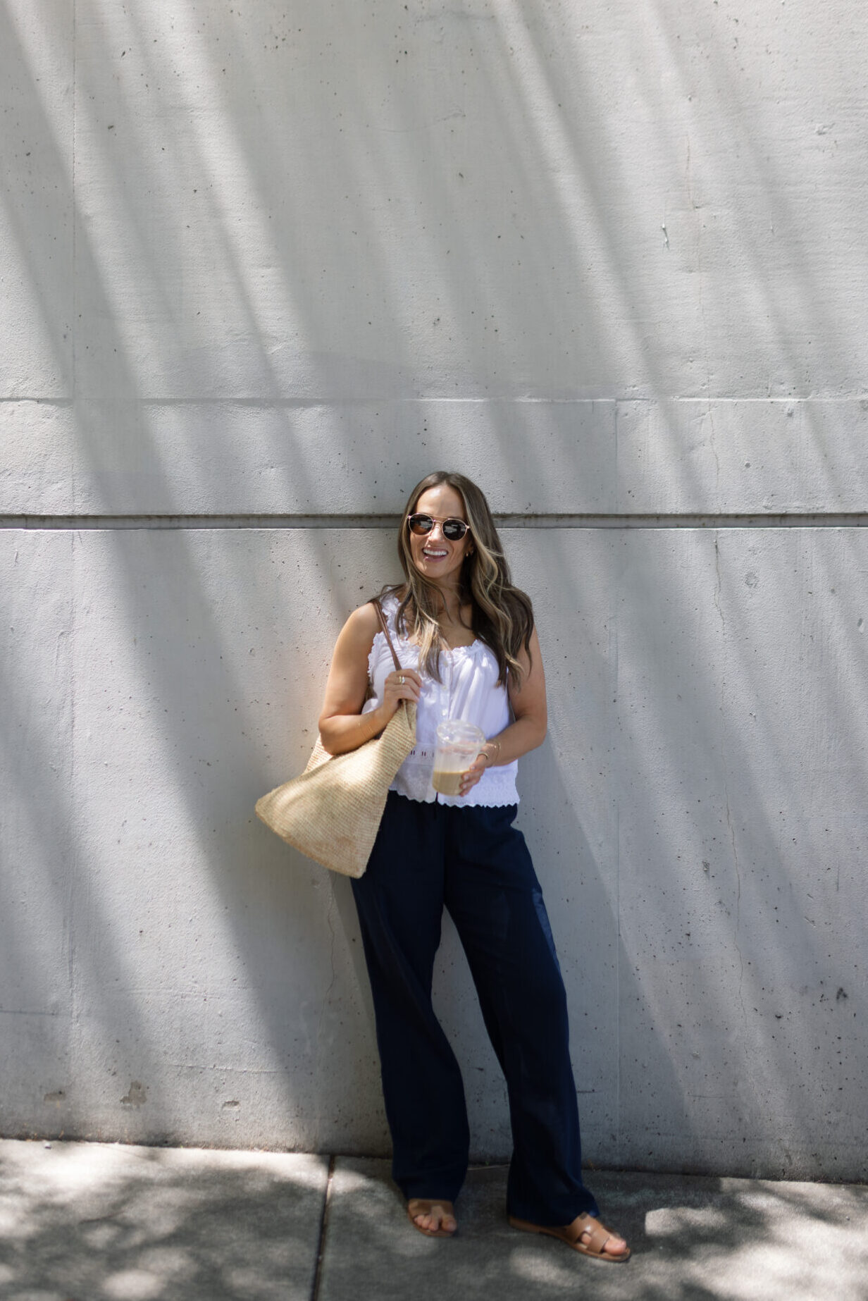 TeriLyn Adams wearing navy linen pants and white tank with sandals and straw bag.