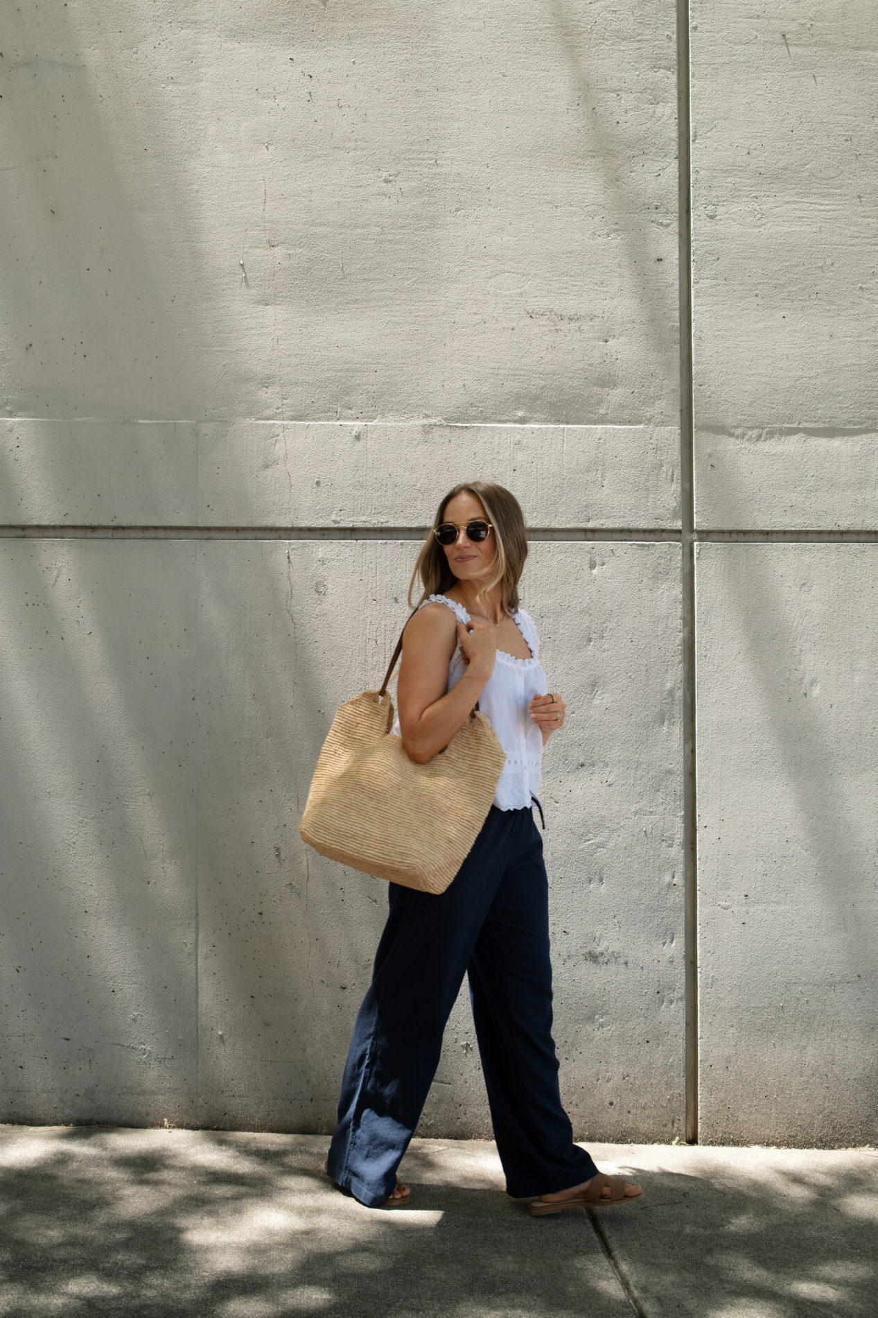 TeriLyn Adams wearing navy linen pants and white tank with sandals and straw bag.