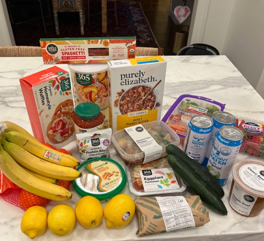 Postpartum snack basket with fruit, waffles, peanut butter, hummus, and easy one-handed foods, flat lay.
