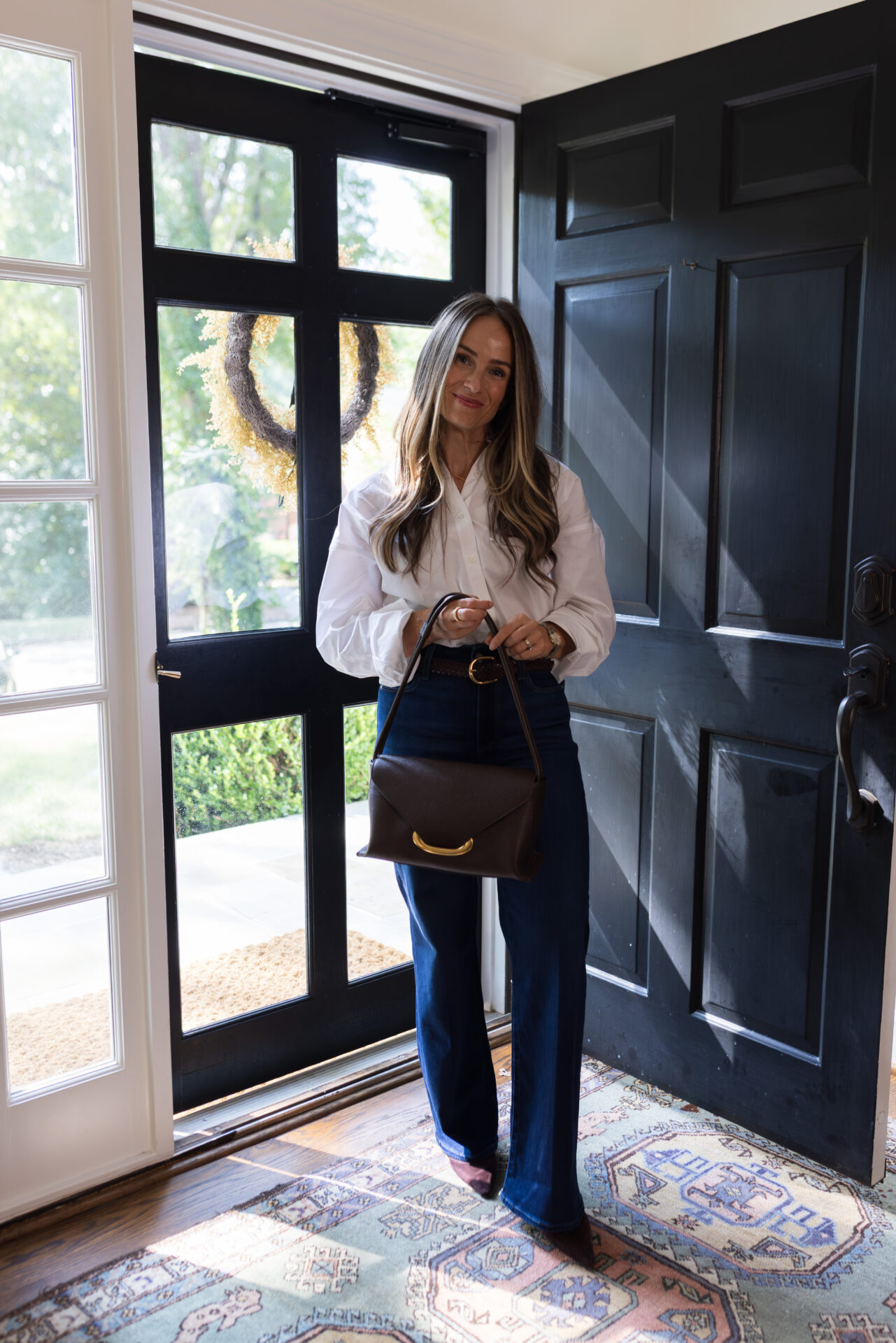 TeriLyn Adams wearing Paige Anessa Wide-Leg Jeans with burgundy suede pumps, a white button-down, and a brown shoulder bag