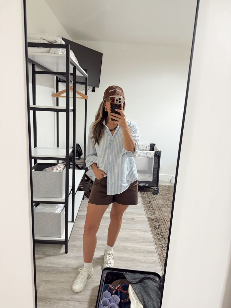TeriLyn Adams wearing brown Madewell Essex Utility Shorts with a blue striped button-down, ball cap, and sneakers