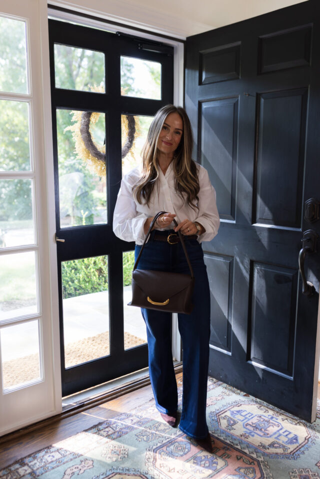 TeriLyn Adams wearing a white button-down, dark wide-leg jeans, and a braided belt with a brown shoulder bag